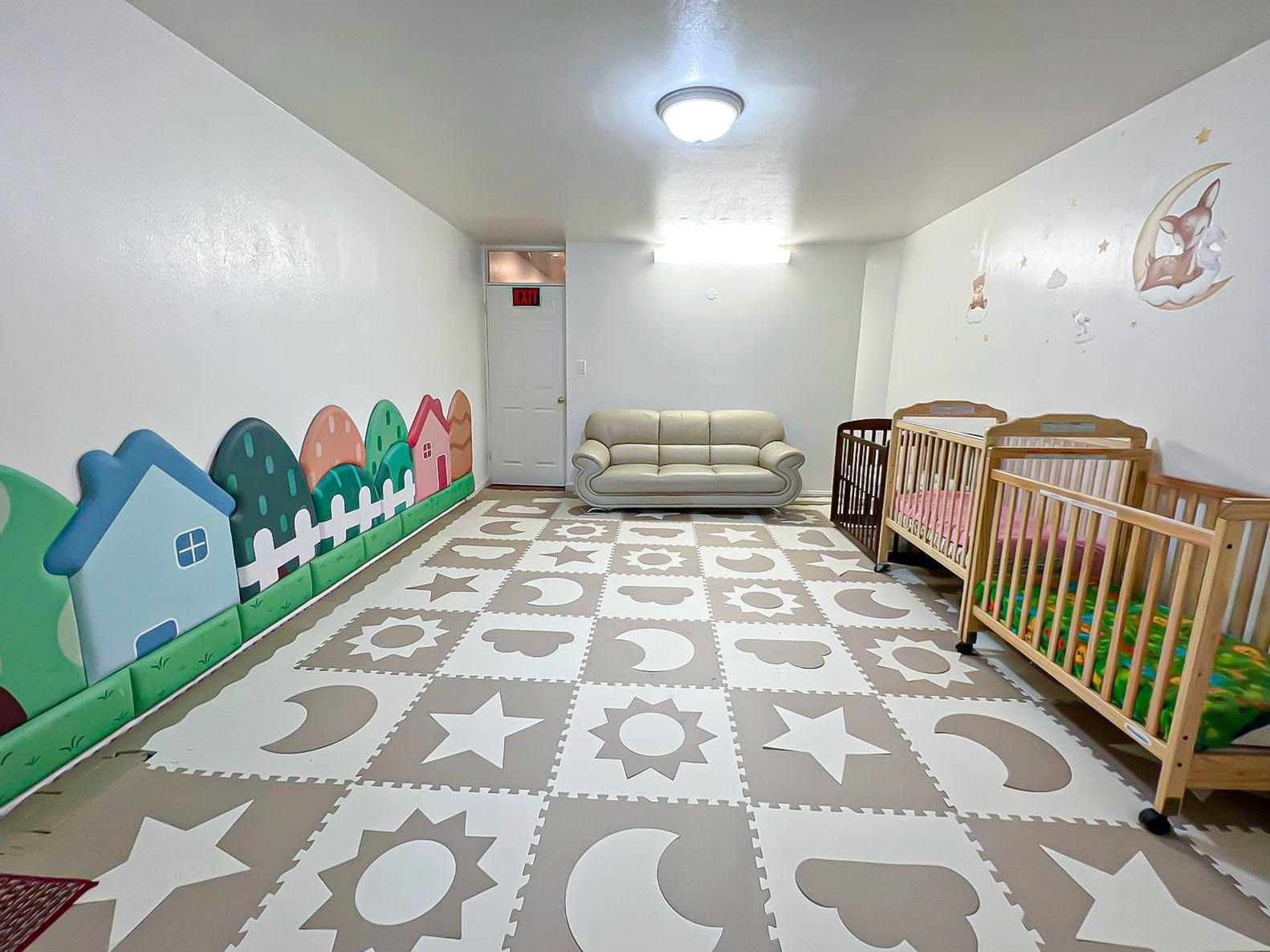 Room with play mat floor, sofa, and two cribs