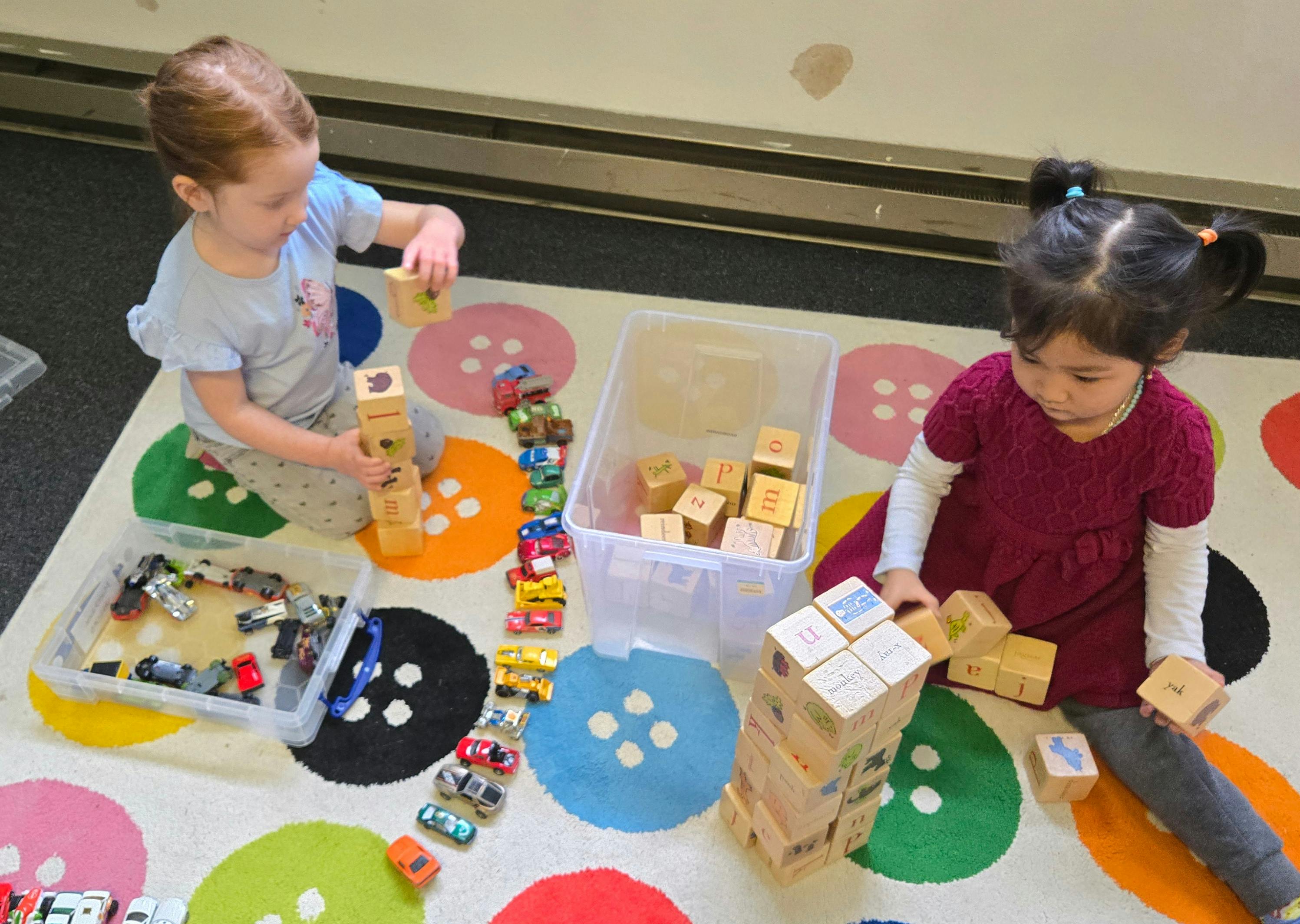 Two children playing with blocks and toy cars on a colorful rug