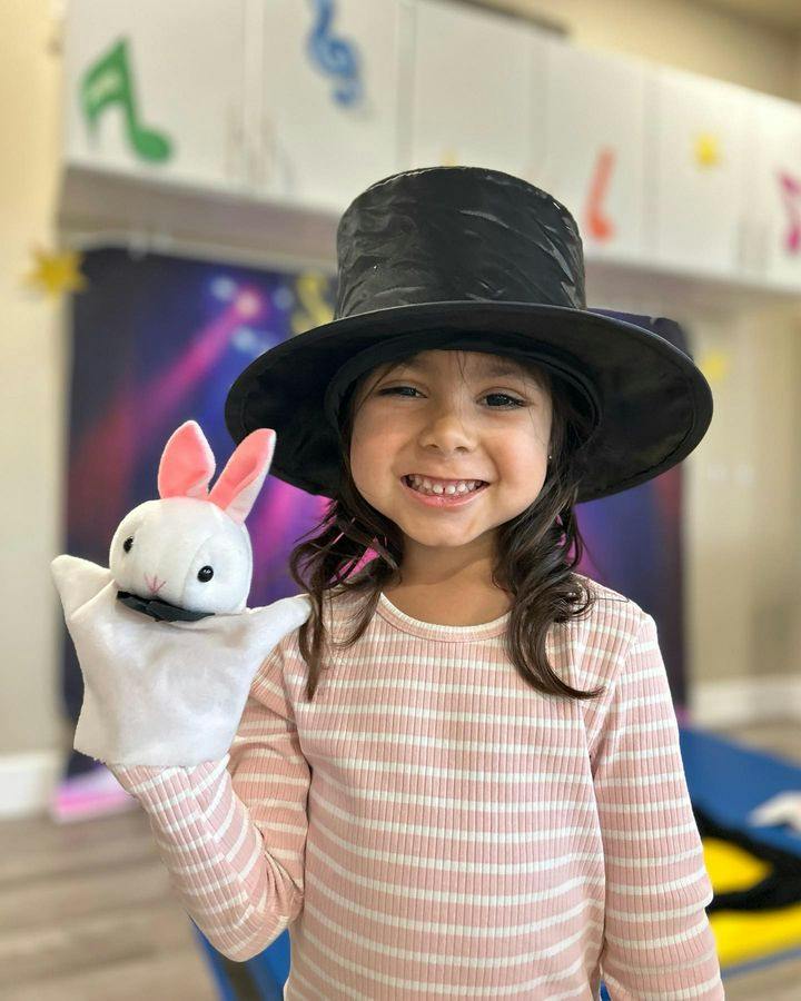Child wearing a top hat and holding a rabbit hand puppet