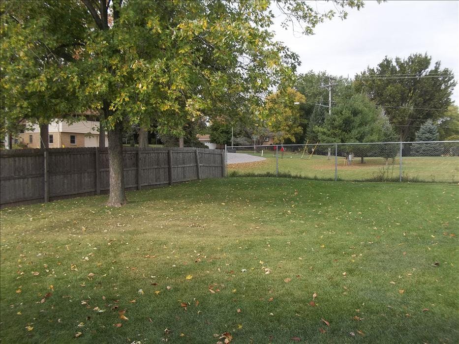 Wooden fence and chain link fence enclosing a grassy yard with trees