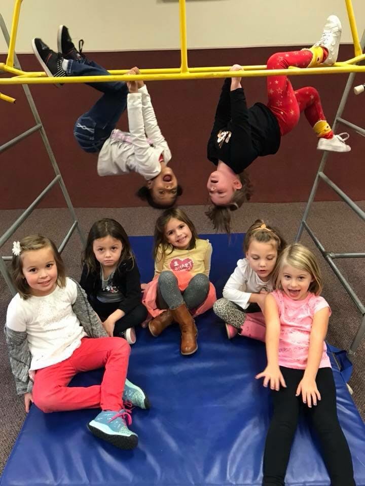 Children playing on a monkey bar and sitting on a blue mat