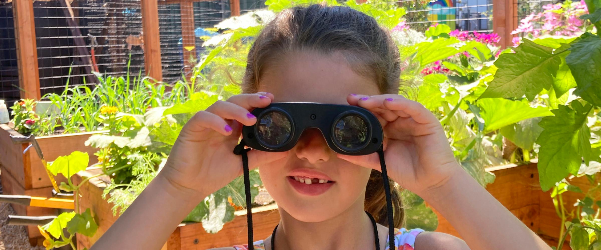Child looking through black toy binoculars