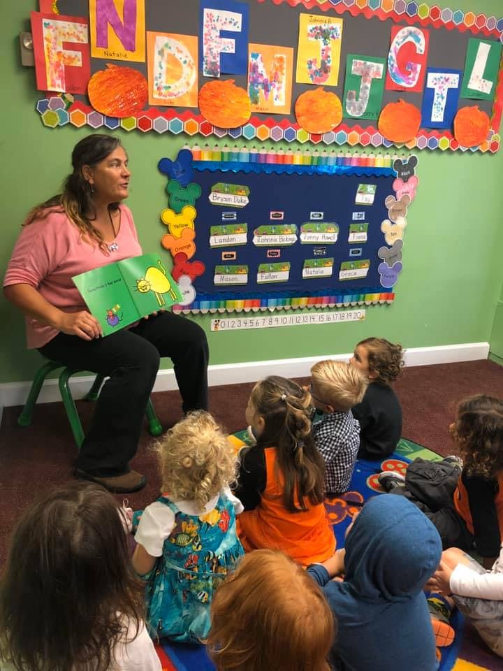 Person reading a book to a group of children in a classroom