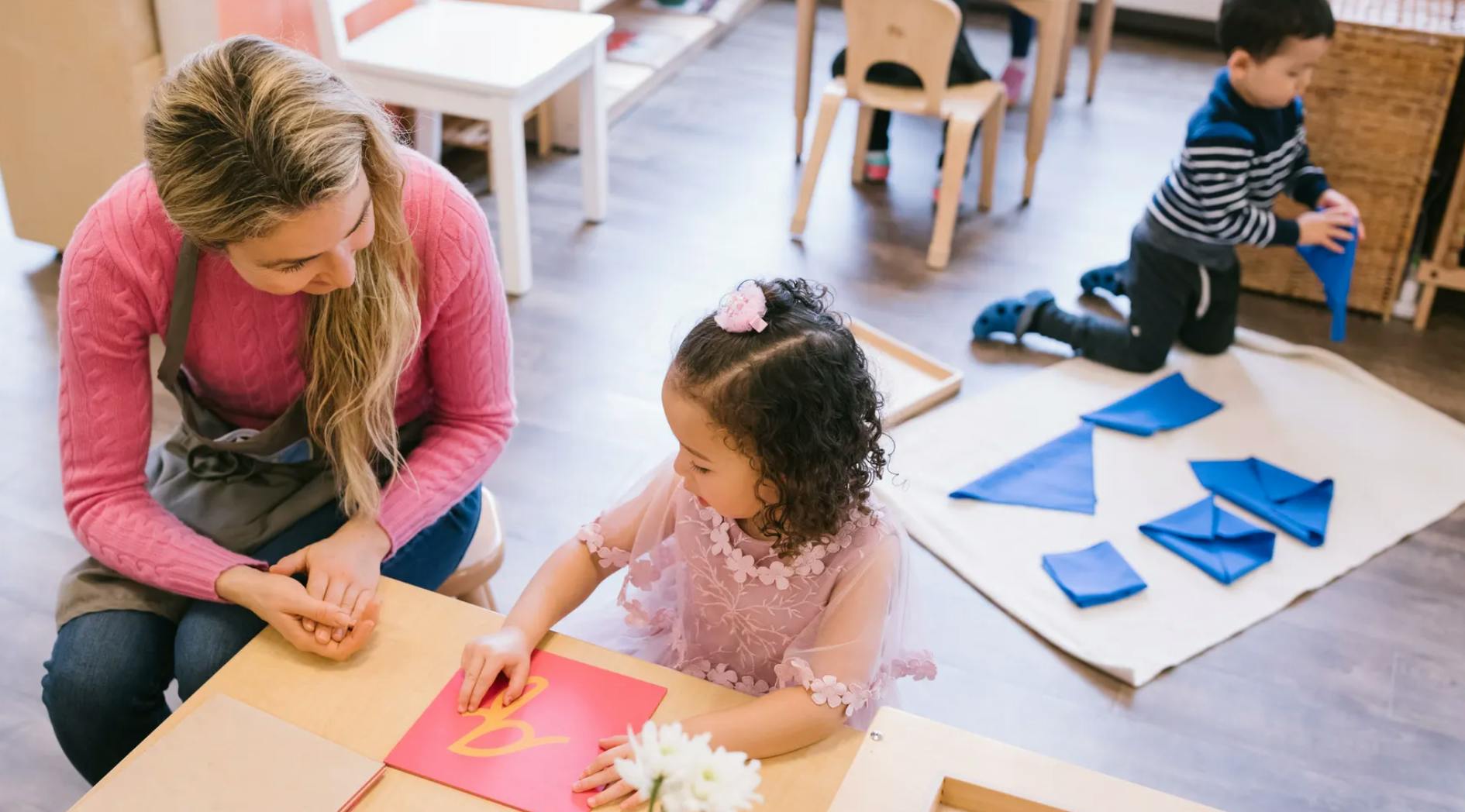 Adult and child at table, another child on floor with shapes