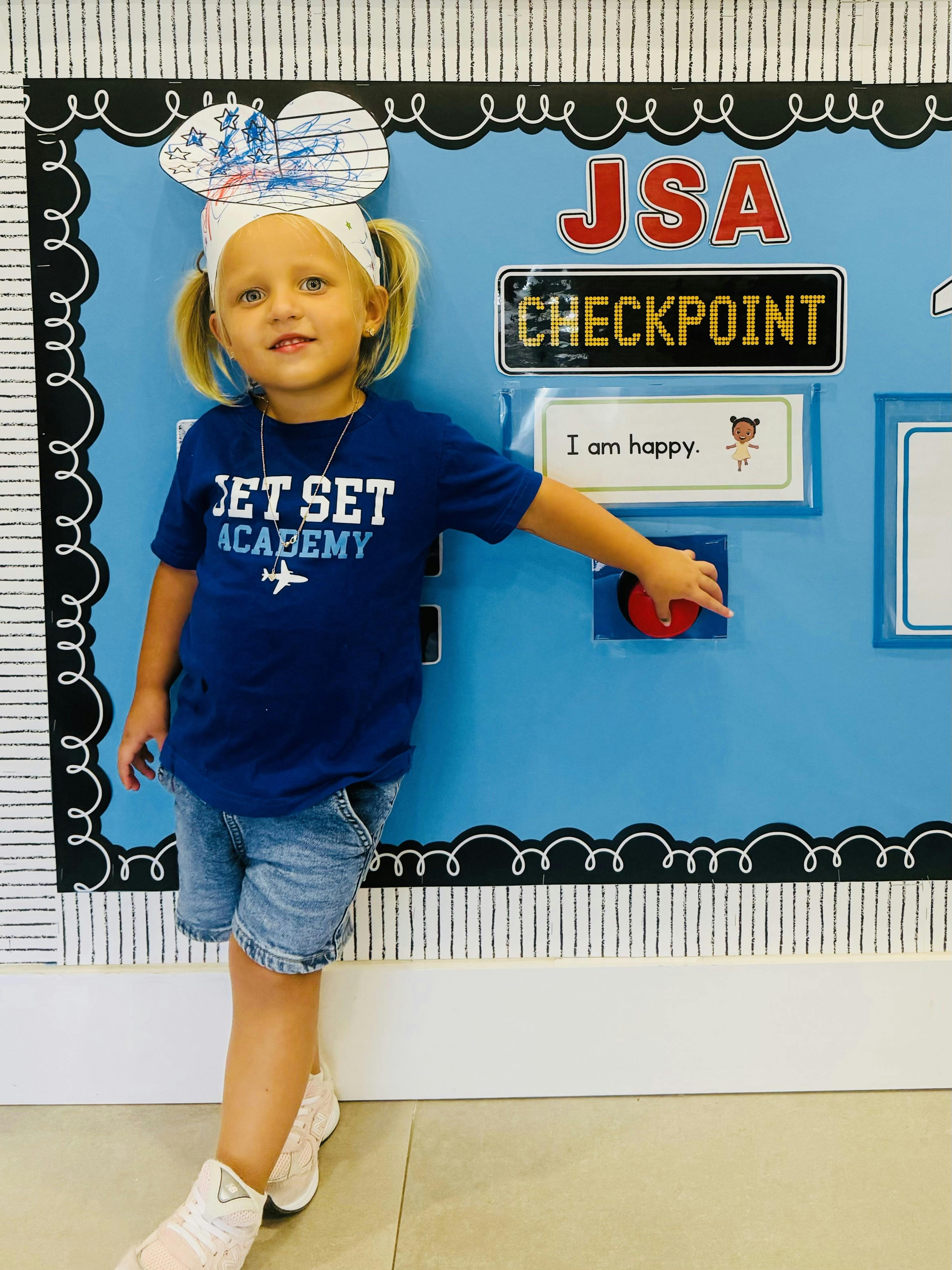Child wearing a paper crown pressing a button on a JSA Checkpoint classroom board