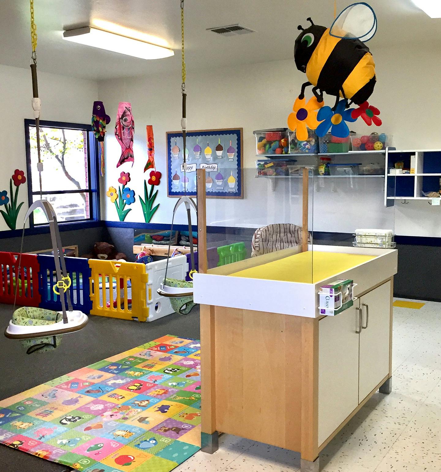 Daycare room with changing table, playpen, and colorful rug