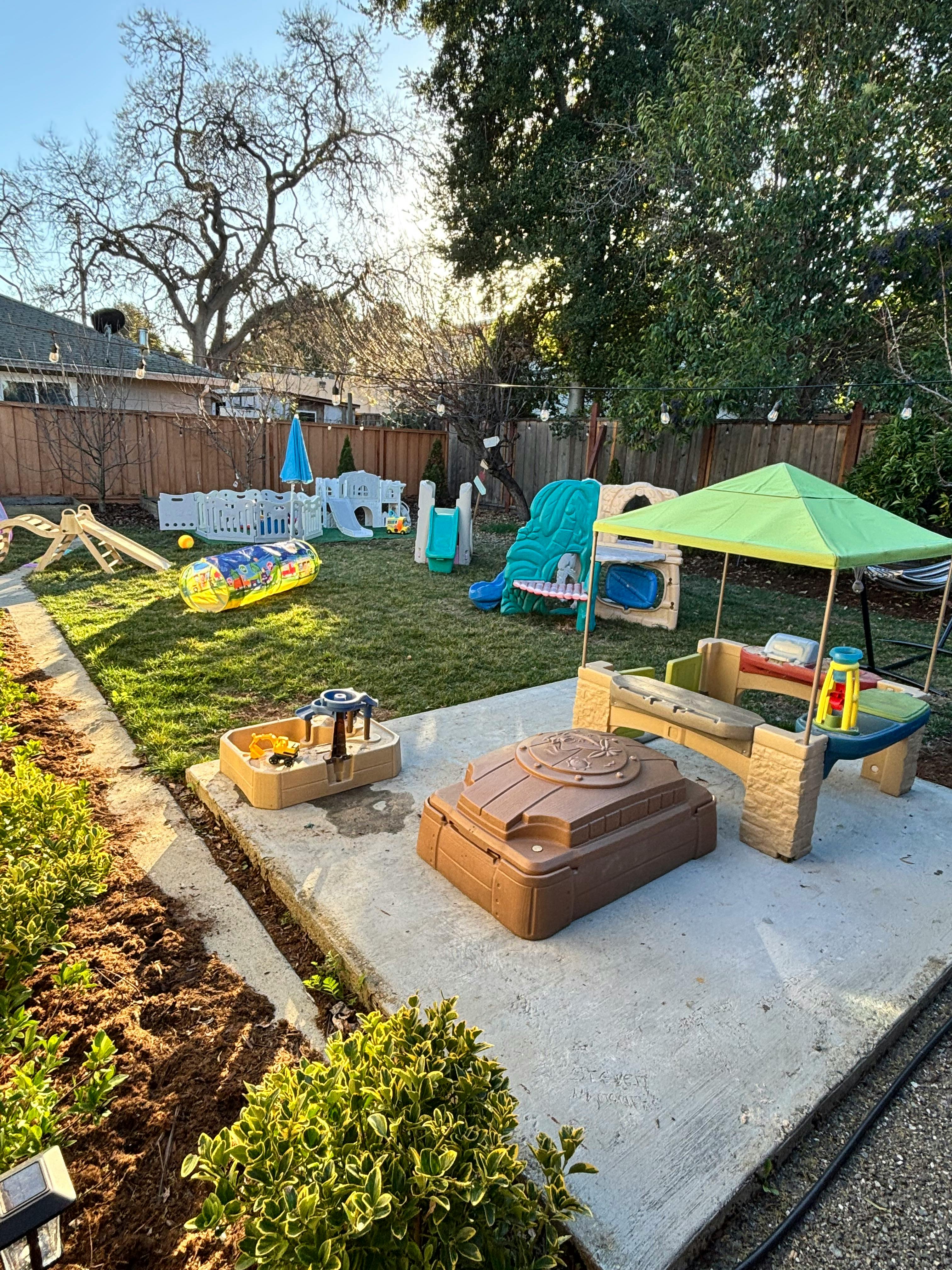 Backyard with various children's play equipment on grass and concrete