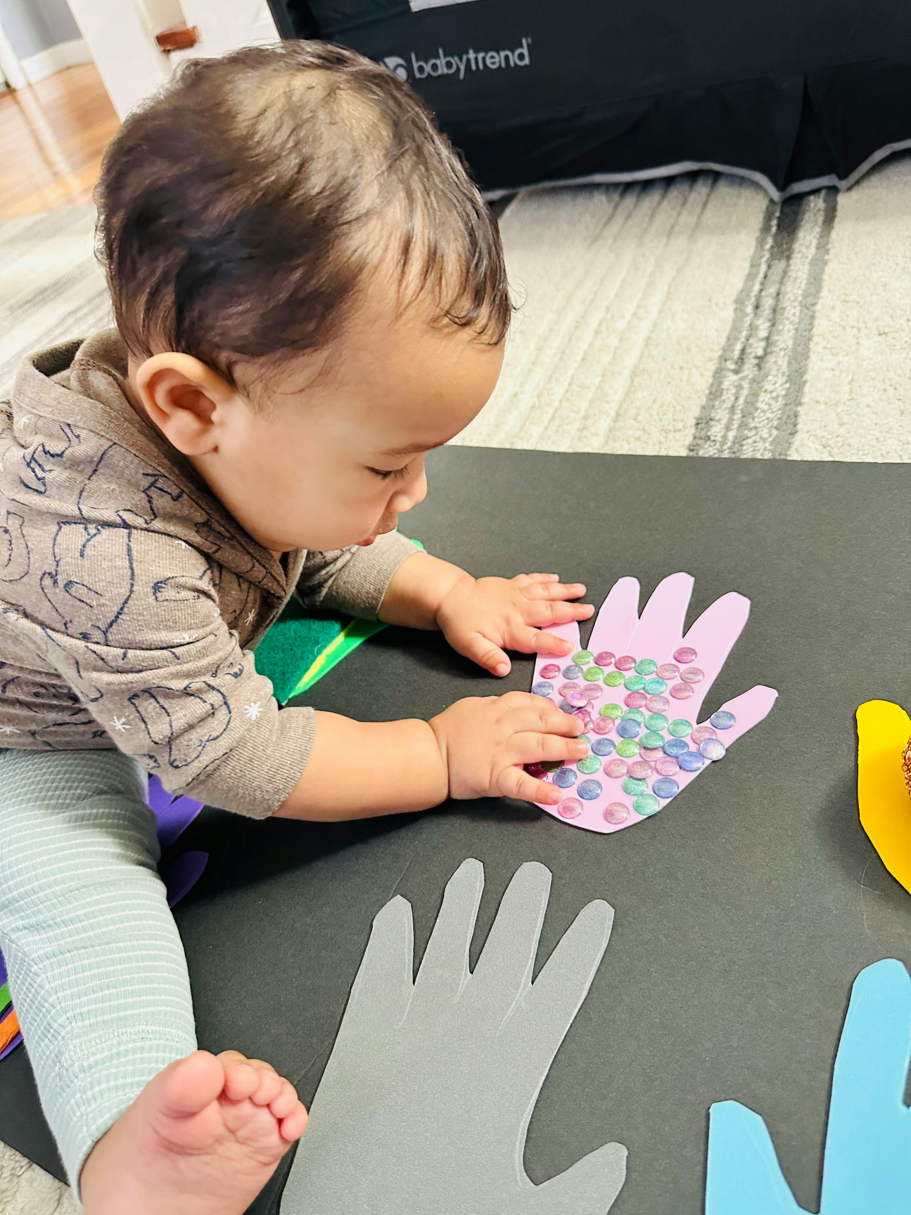 Child playing with paper hand cutouts decorated with small colorful circles
