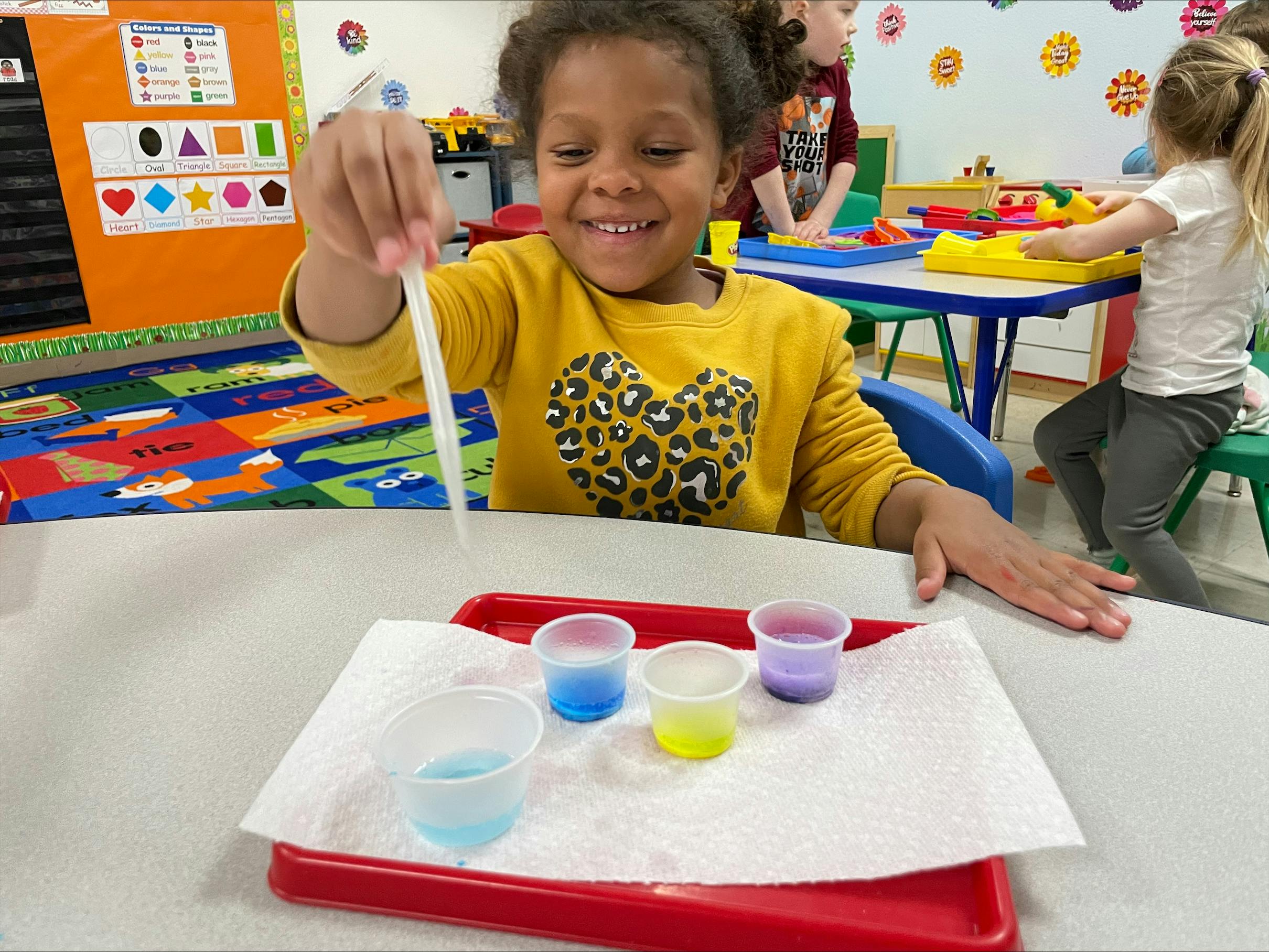 Child using a dropper with small cups of colored liquid in a classroom