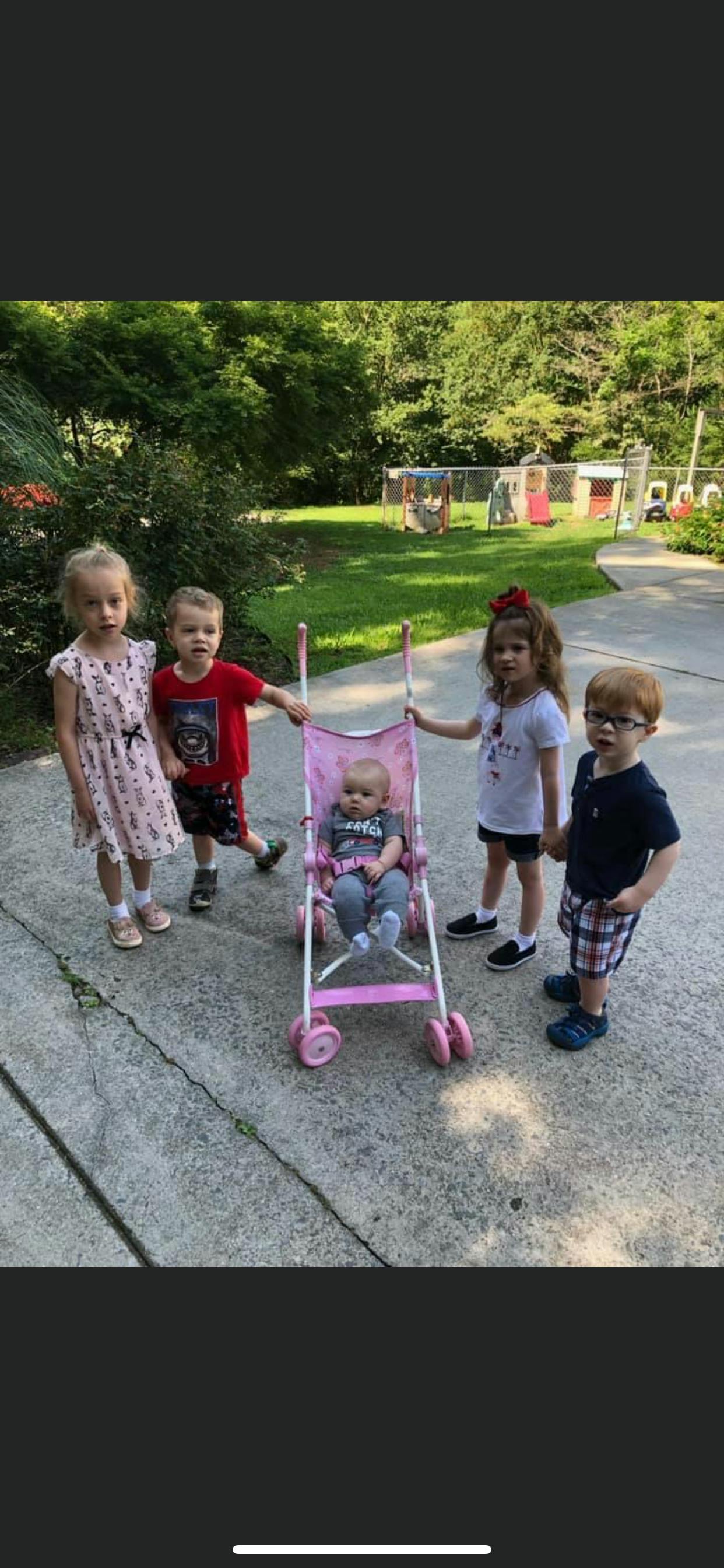Four children standing around a baby in a pink stroller outdoors