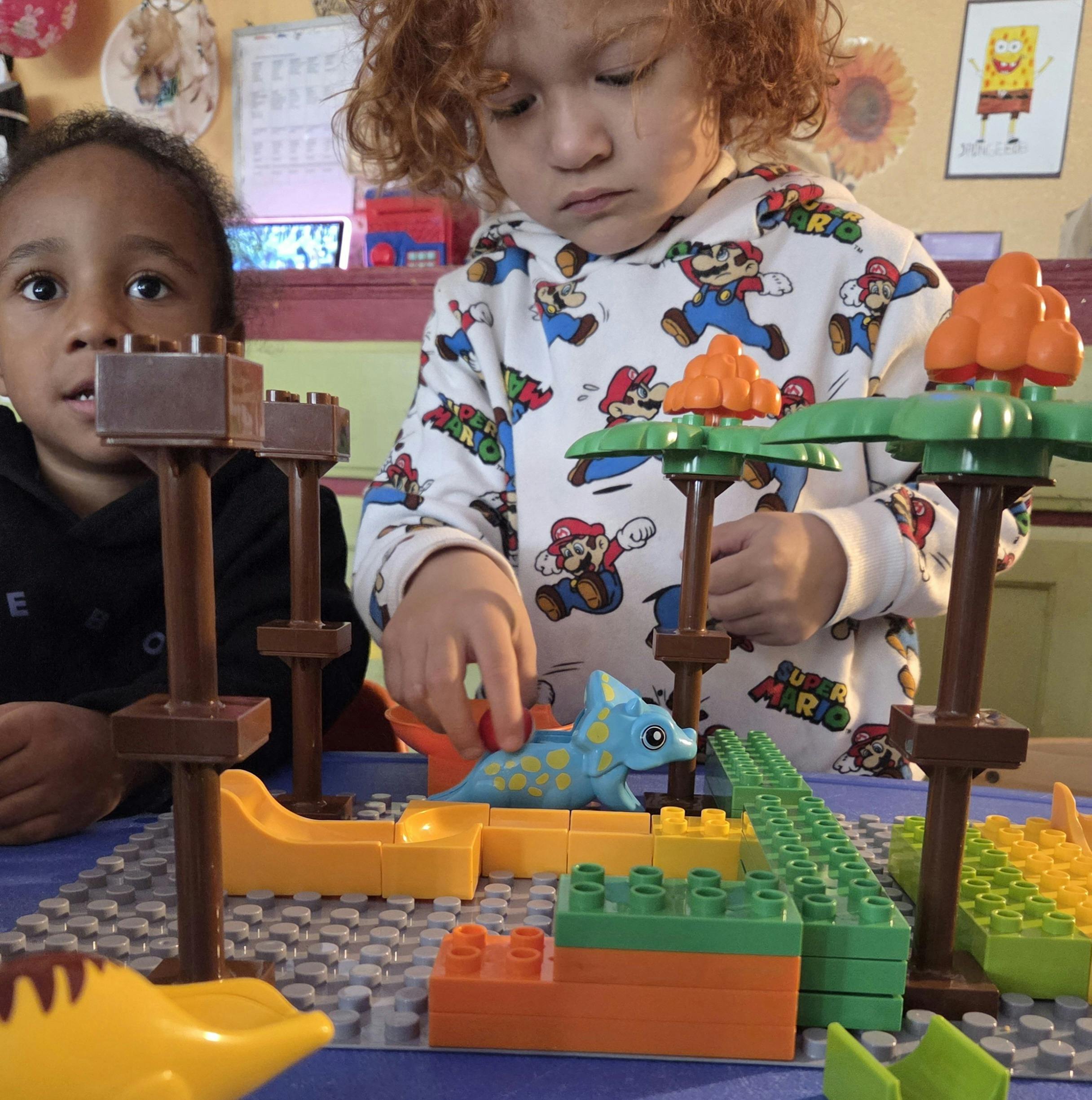 Two children playing with building blocks and toy dinosaurs