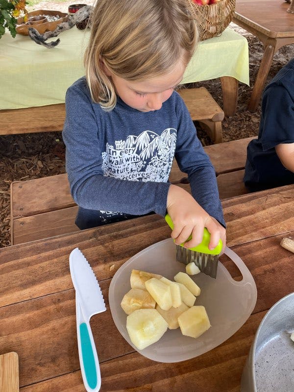 Child cutting pieces of fruit on a cutting board