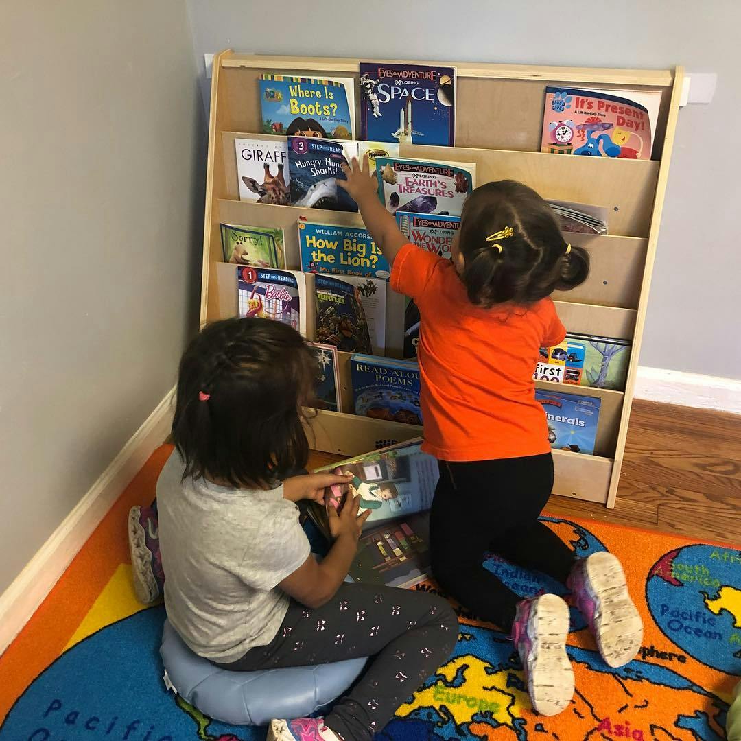 Two children looking at books on a shelf and on the floor