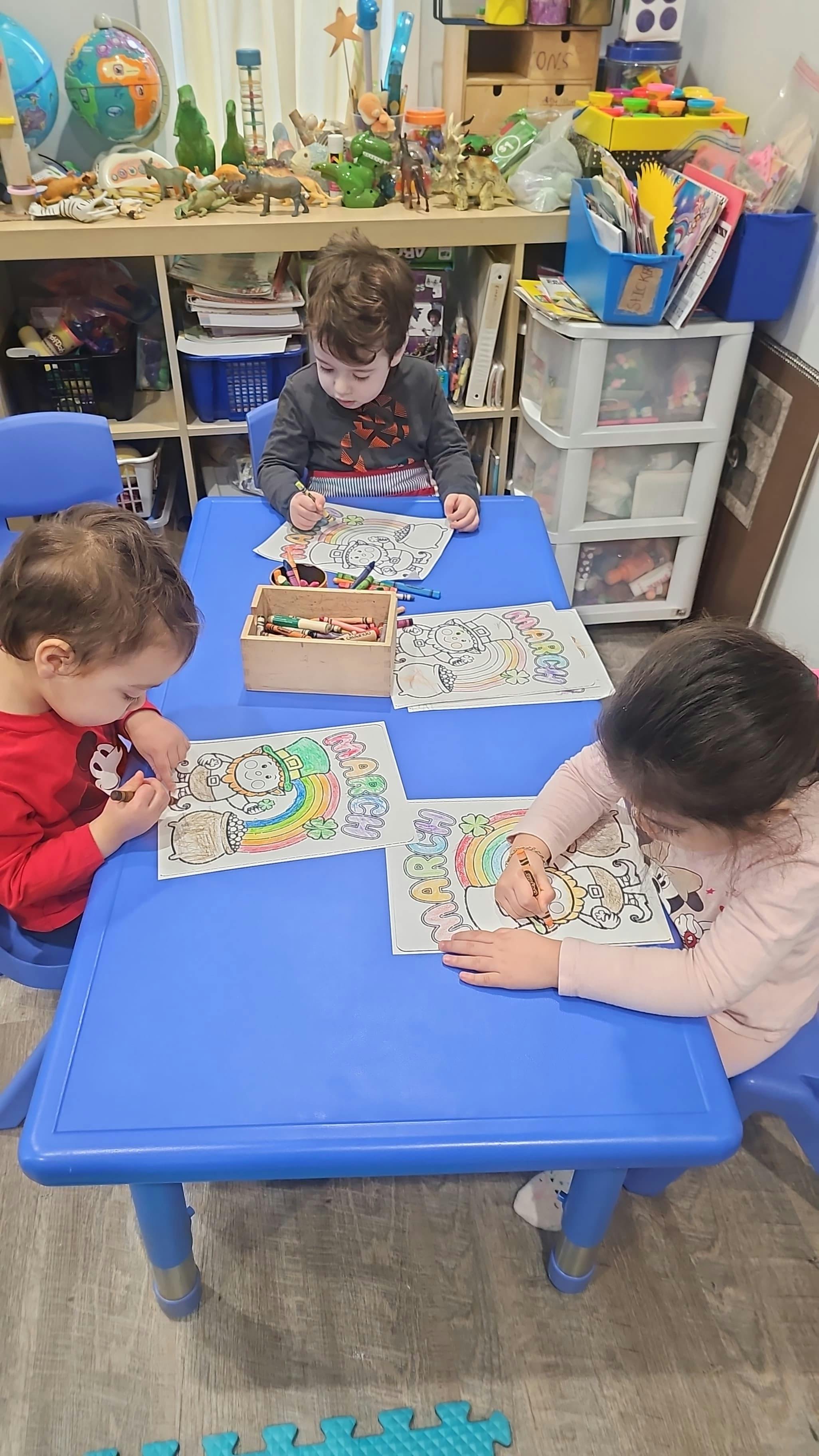 Three children coloring March-themed pictures at a blue table