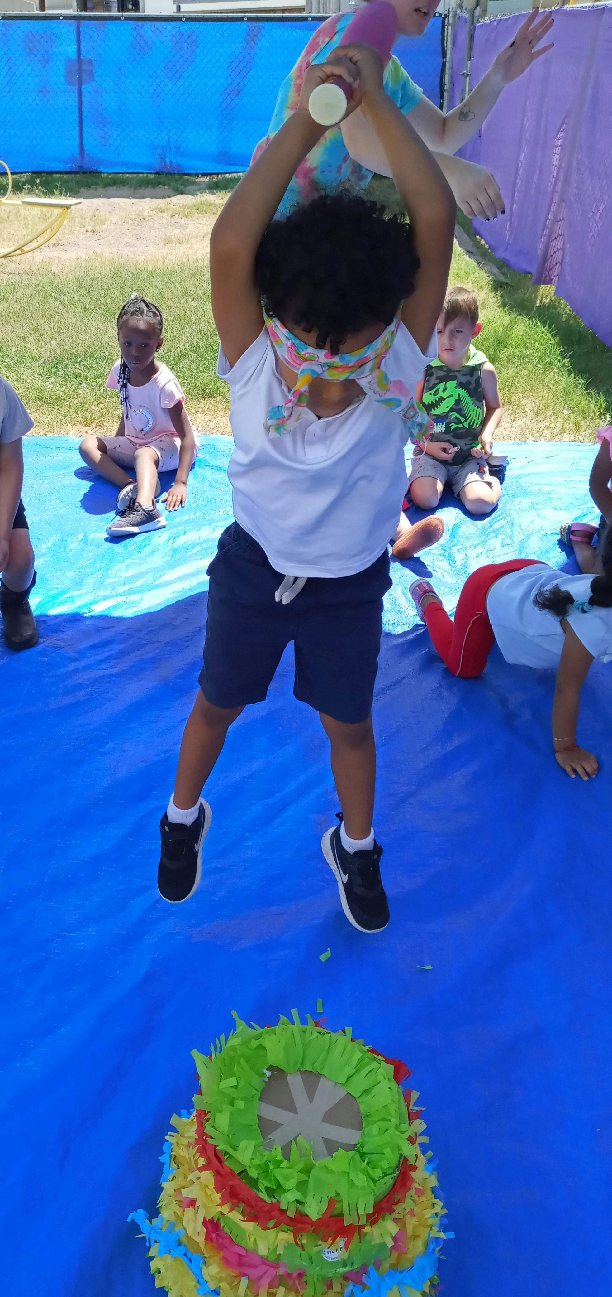 Child blindfolded, holding a stick over a colorful piñata