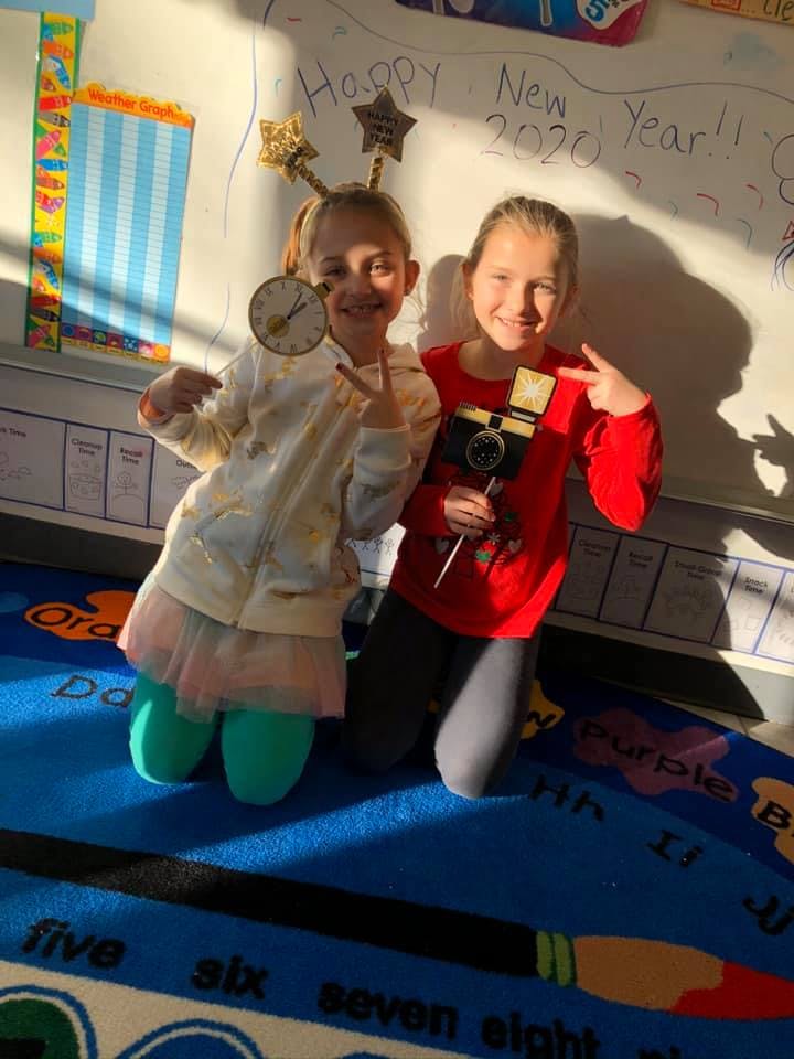 Two children kneeling and posing in front of a whiteboard