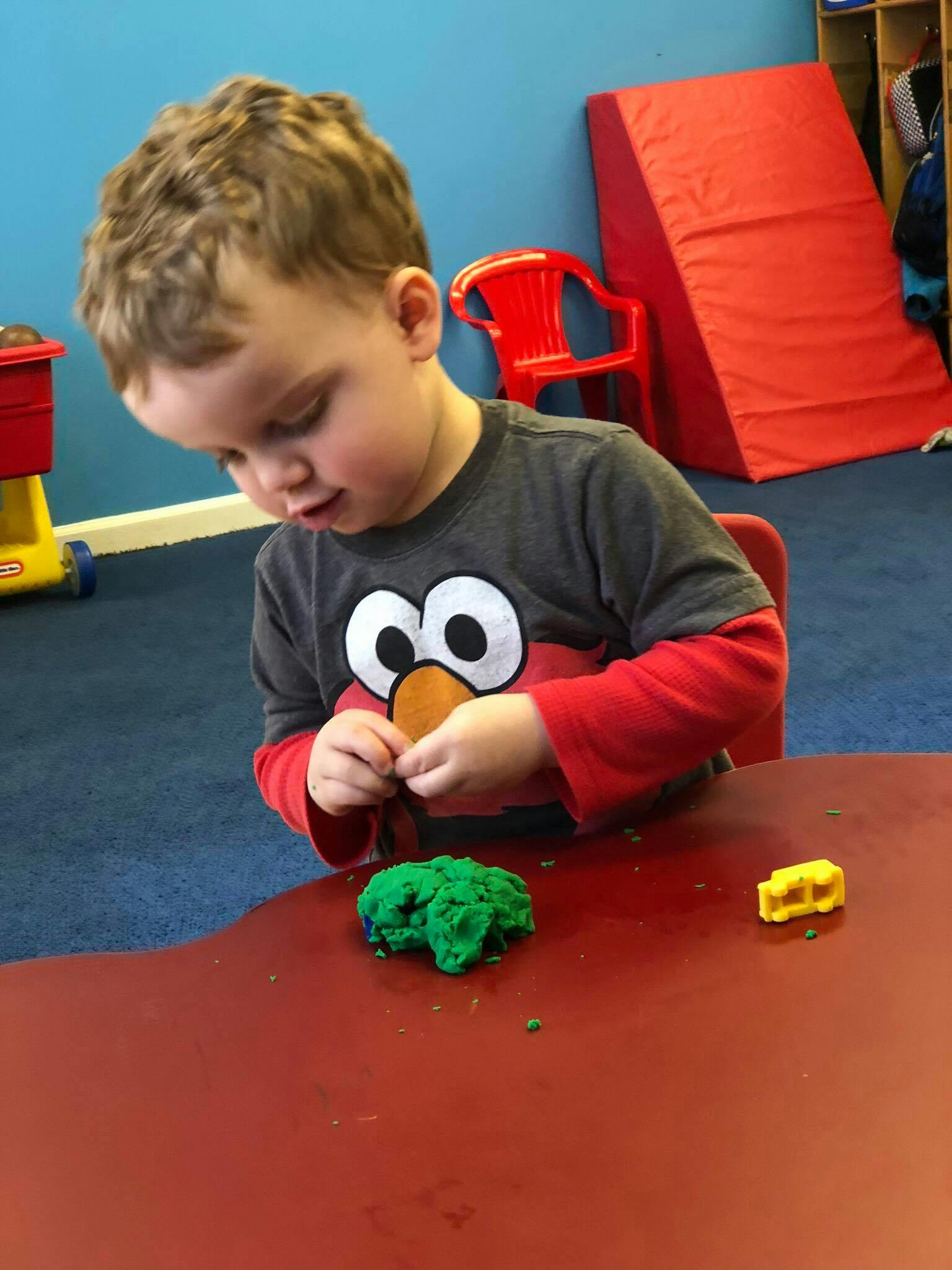 Child playing with green playdough at a table