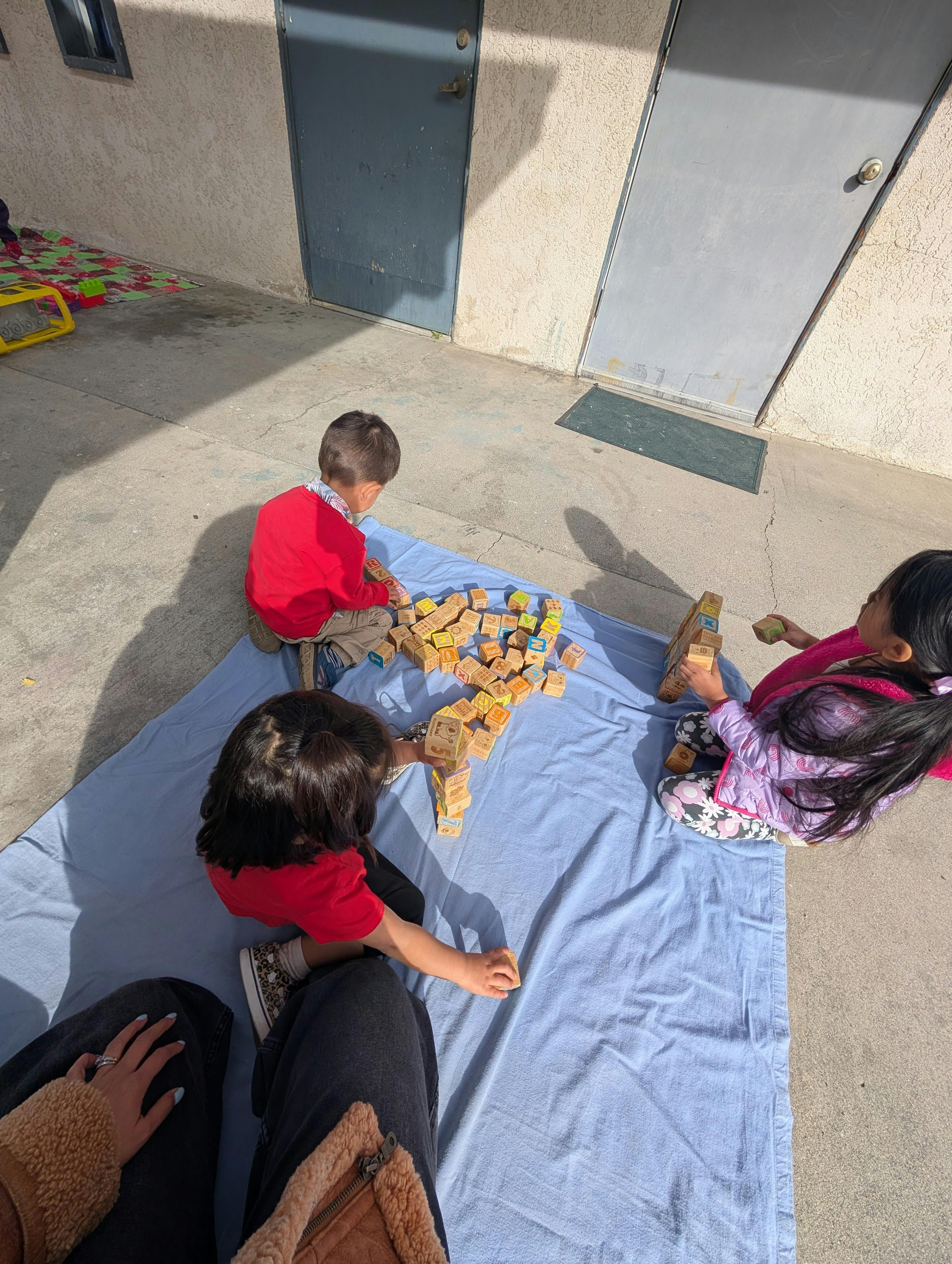 Three children playing with wooden alphabet blocks on a blue blanket