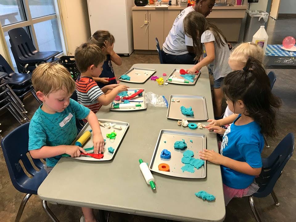 Children and adults at a table playing with modeling clay