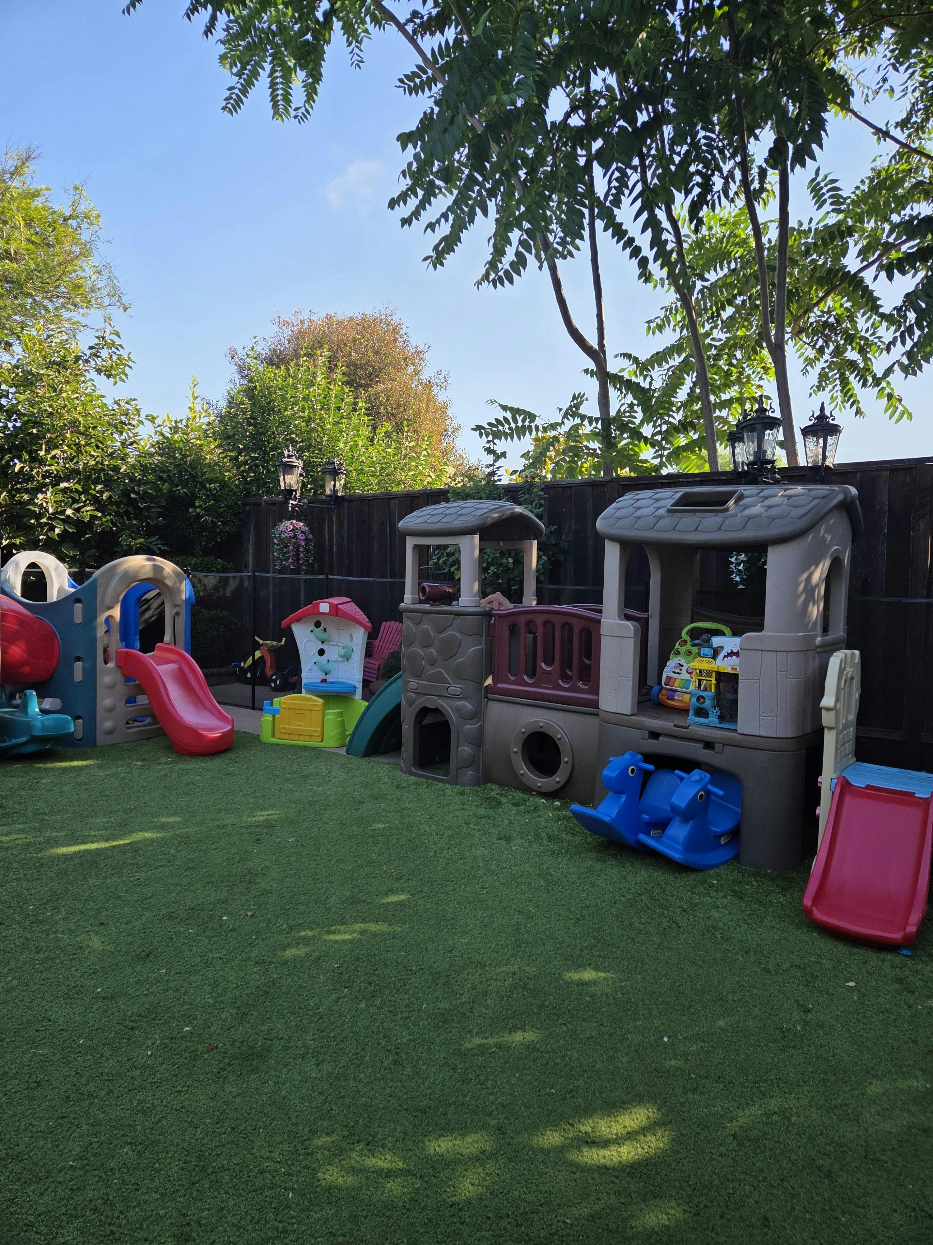 A backyard play area with multiple plastic play structures and slides on artificial turf