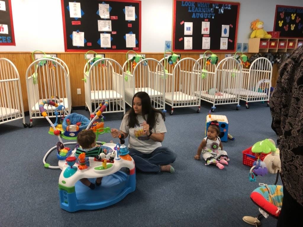 Person sitting on floor with two children and baby activity center in a room with cribs
