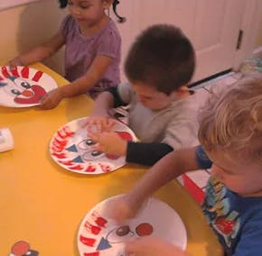 Three children making crafts with paper plates at a table