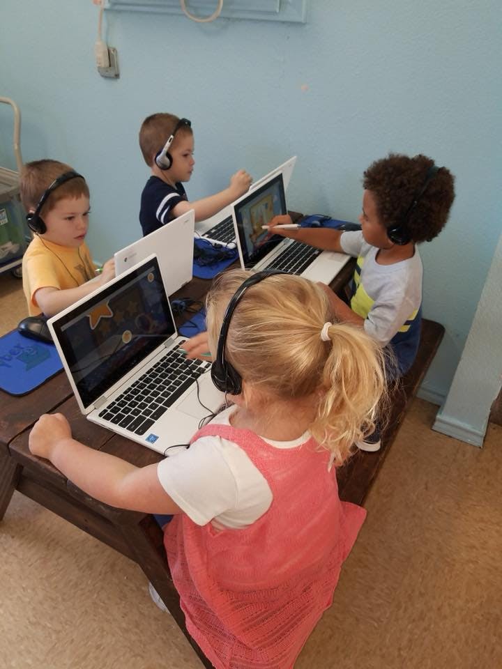 Children wearing headphones using laptops in a classroom