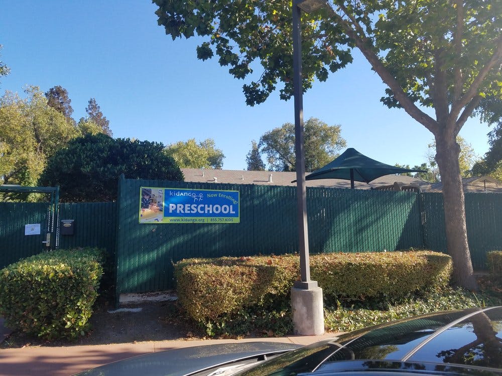 Preschool sign on a green fence with bushes and trees