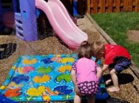 Two children playing with a water mat on a playground