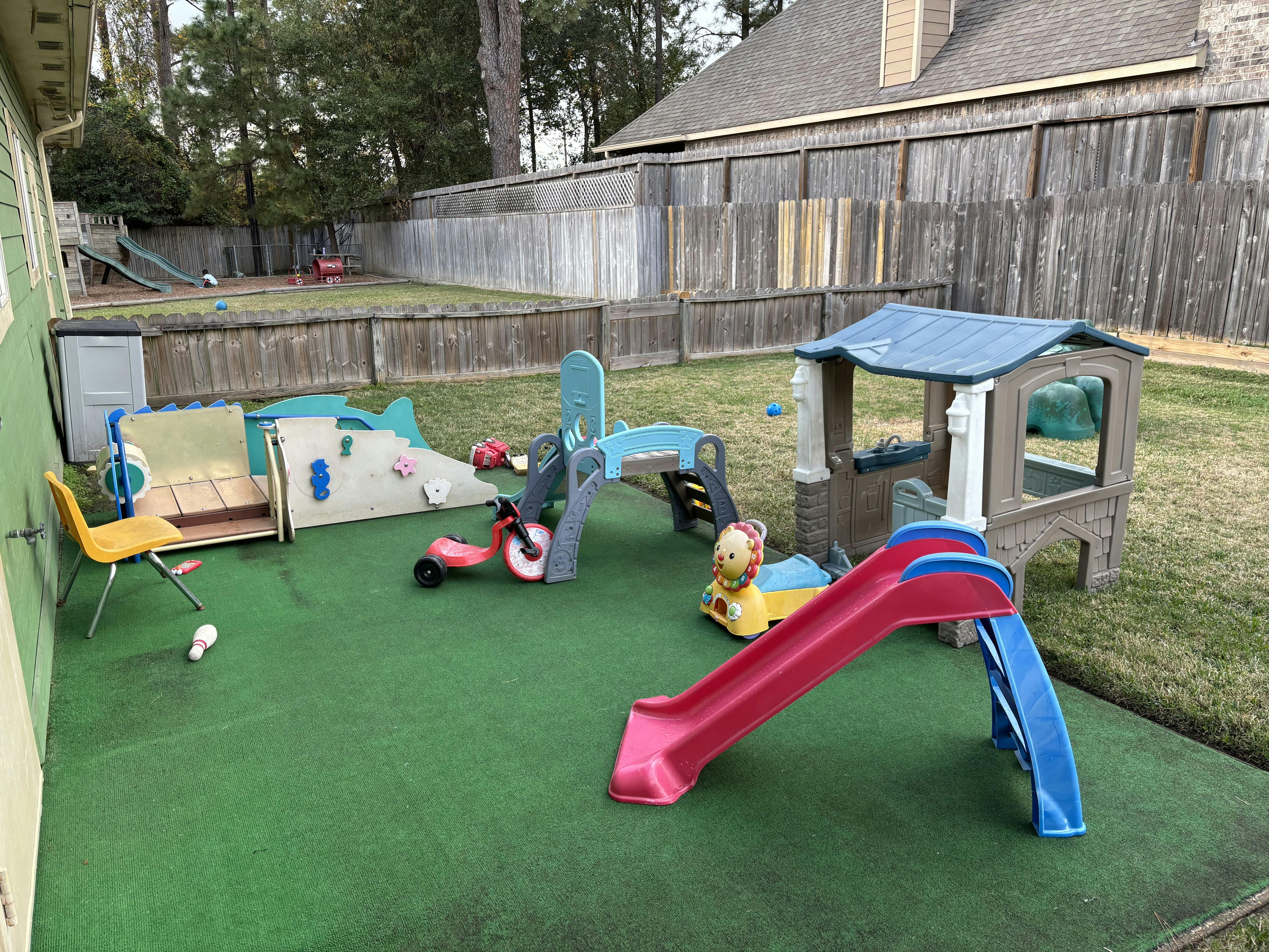 Outdoor play area with slides, playhouses, and ride-on toys on green turf