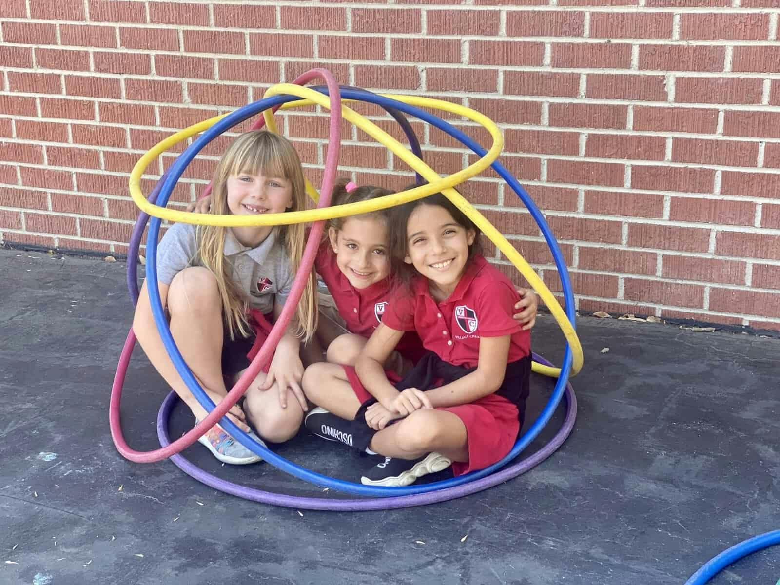 Three children sitting inside intertwined hula hoops on a playground