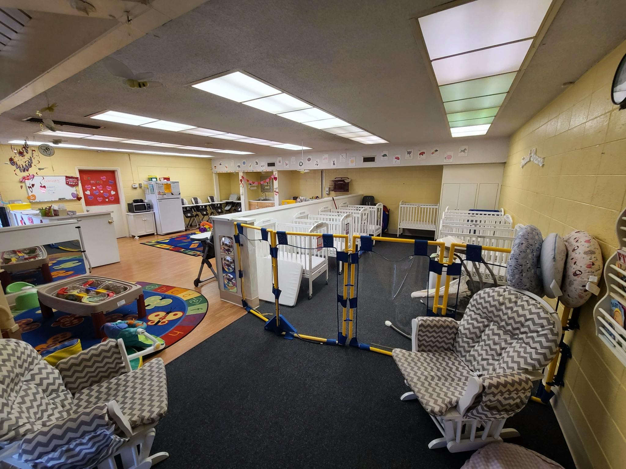 Daycare room with play area, cribs, and rocking chairs