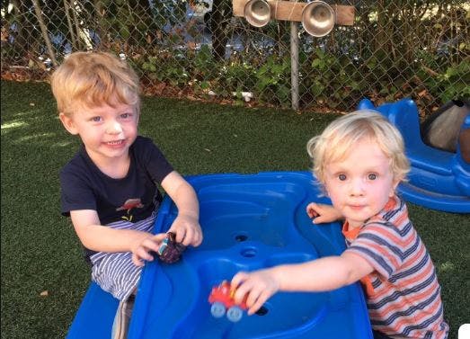Two children playing with toy cars on a blue play structure