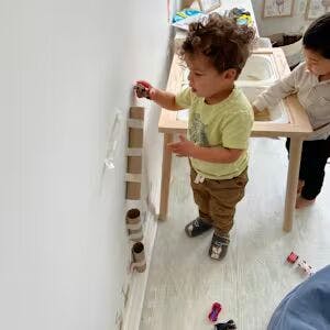 Child playing with toy cars and cardboard tubes taped to a wall
