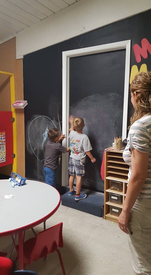 Two children drawing on a chalkboard in a classroom