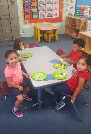 Four children eating at a table in a classroom