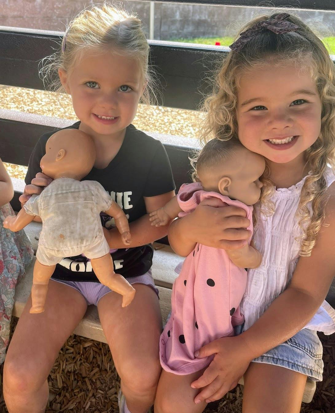 Two children sitting together and holding baby dolls