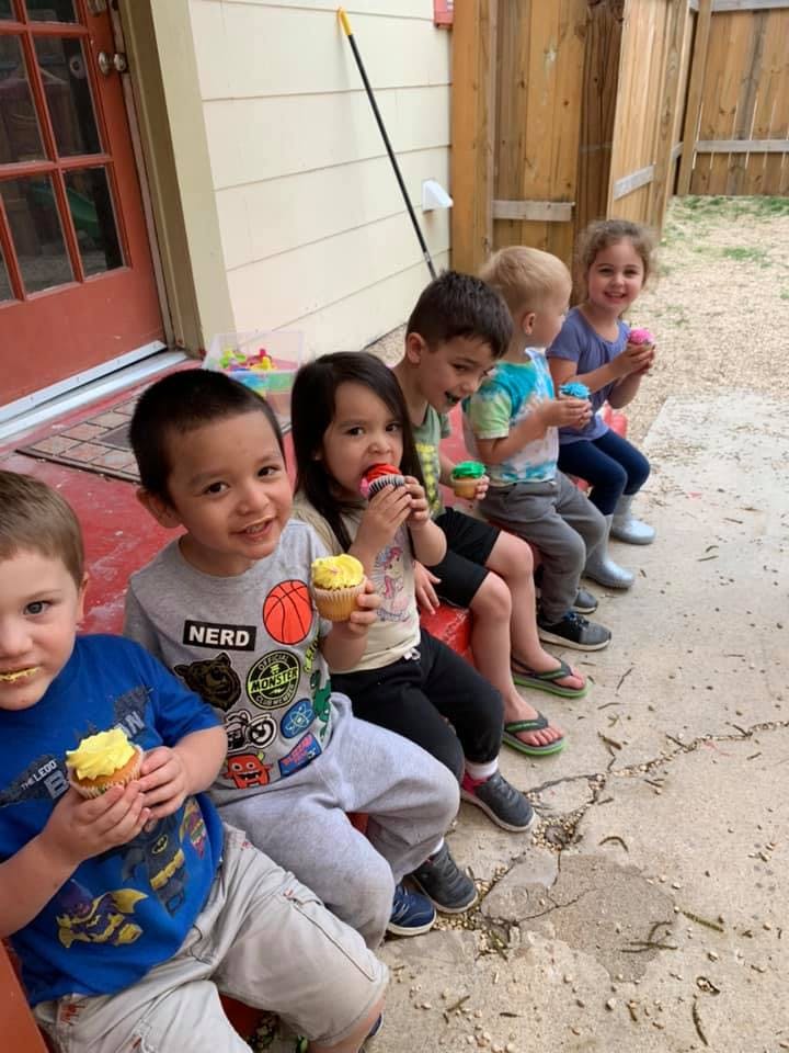 Children sitting in a row eating cupcakes outdoors