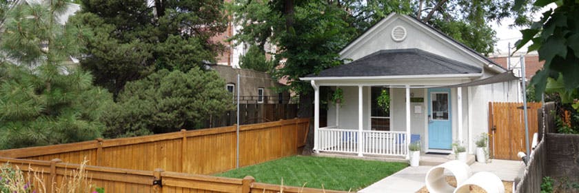 Small house with a porch and a light blue door, surrounded by a wooden fence