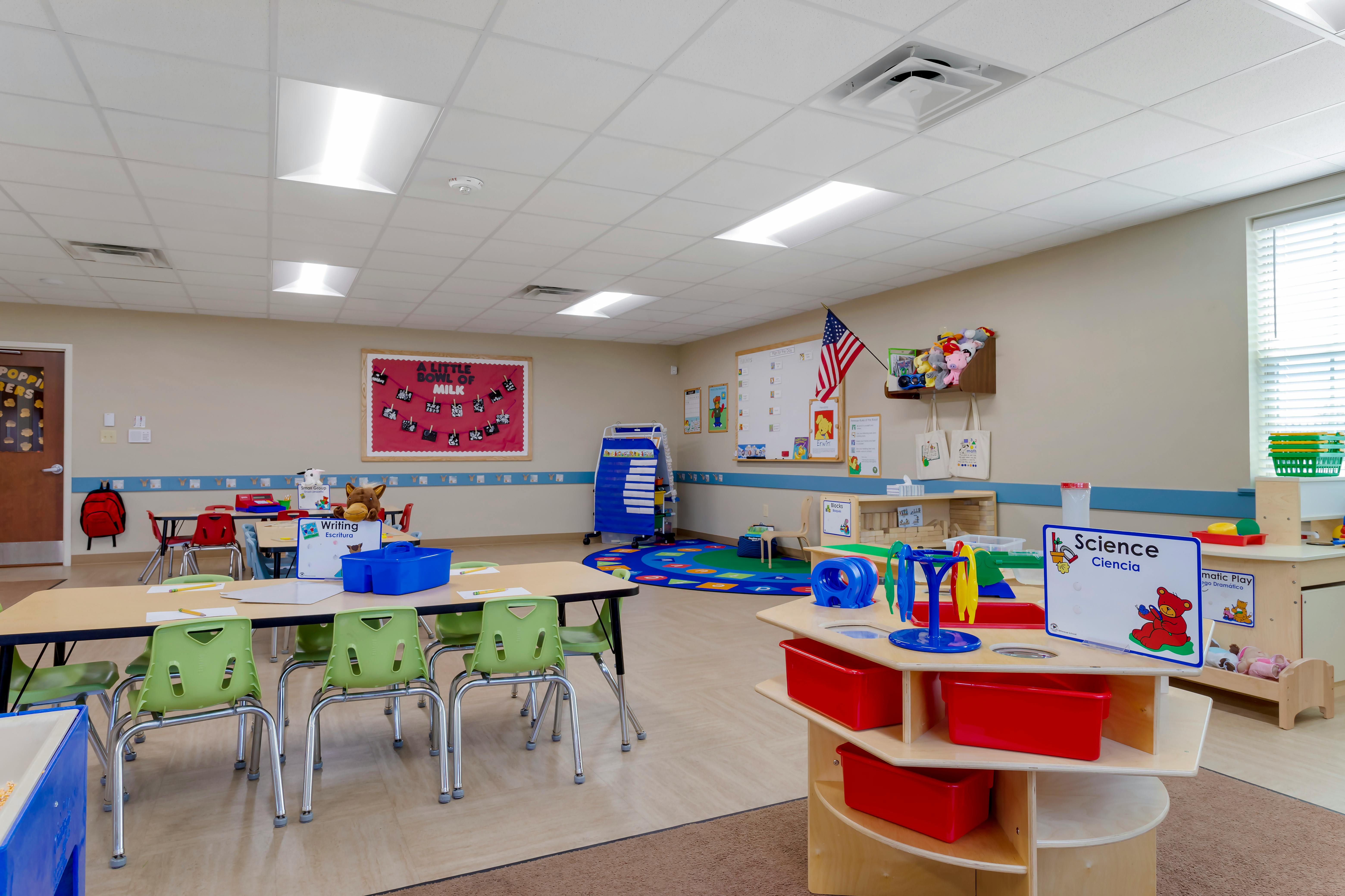 Classroom with child-sized tables and chairs, a play rug, and learning stations