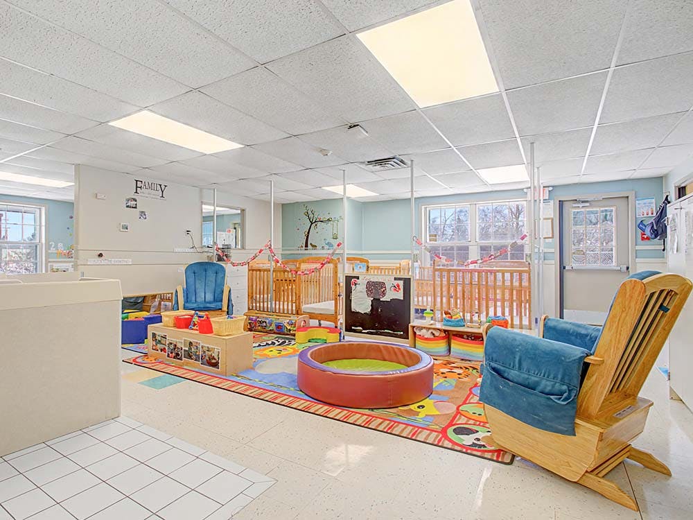 Childcare room with cribs, play mat, and rocking chair