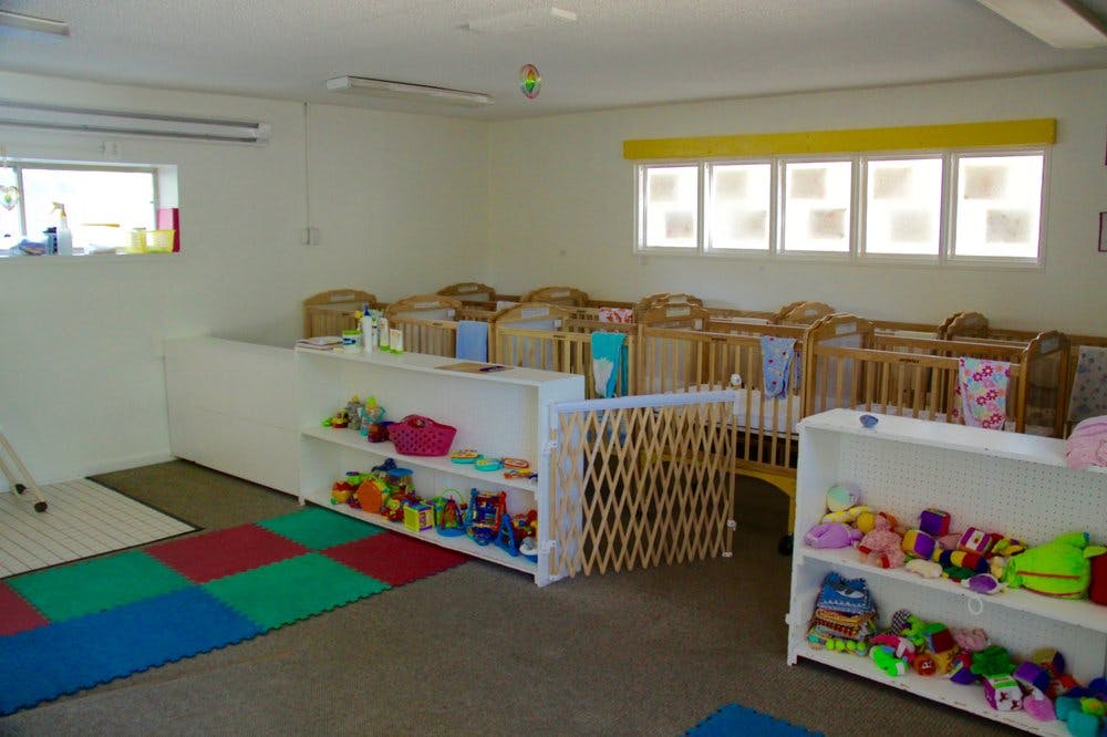 Room with multiple cribs, shelves with toys, and a play mat