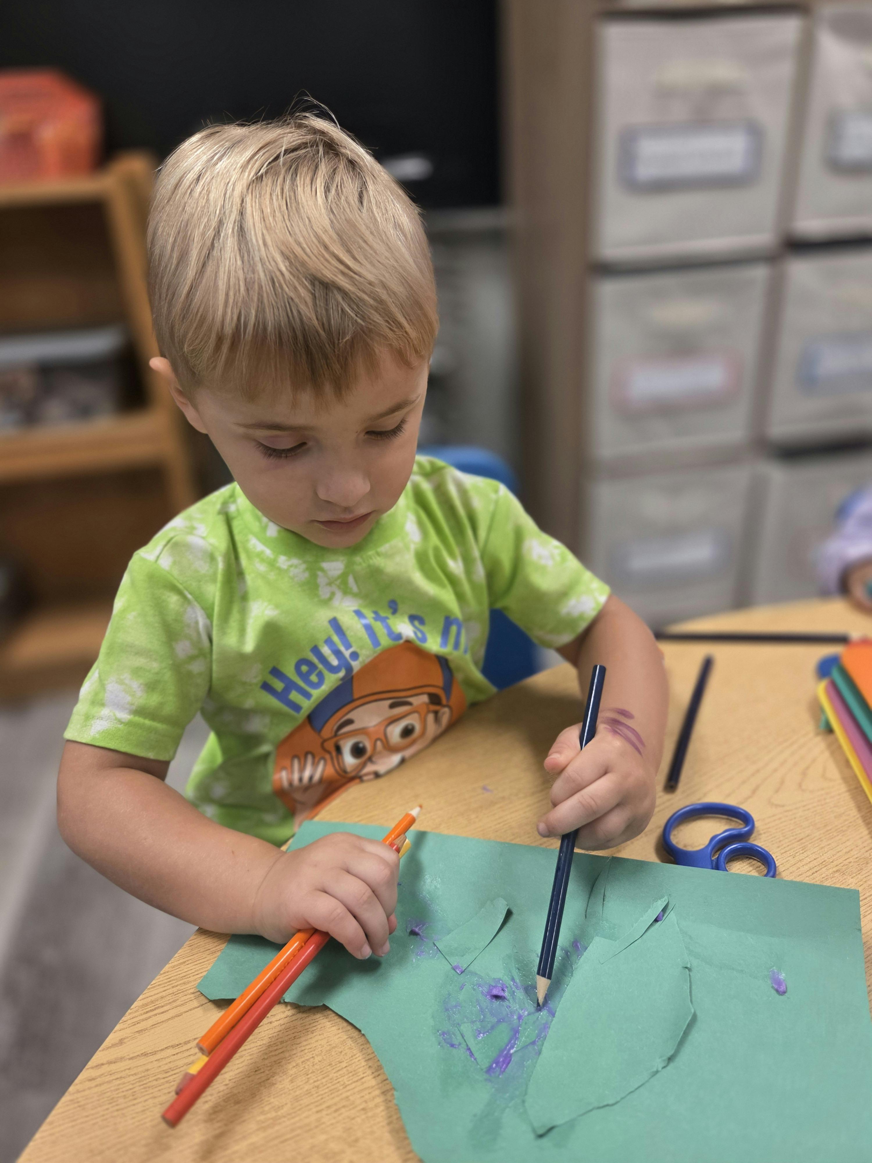 Child coloring green paper with pencils in-image text "Hey! It's n"