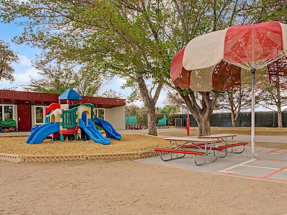 Colorful playground with multiple slides next to picnic tables and a red and white umbrella