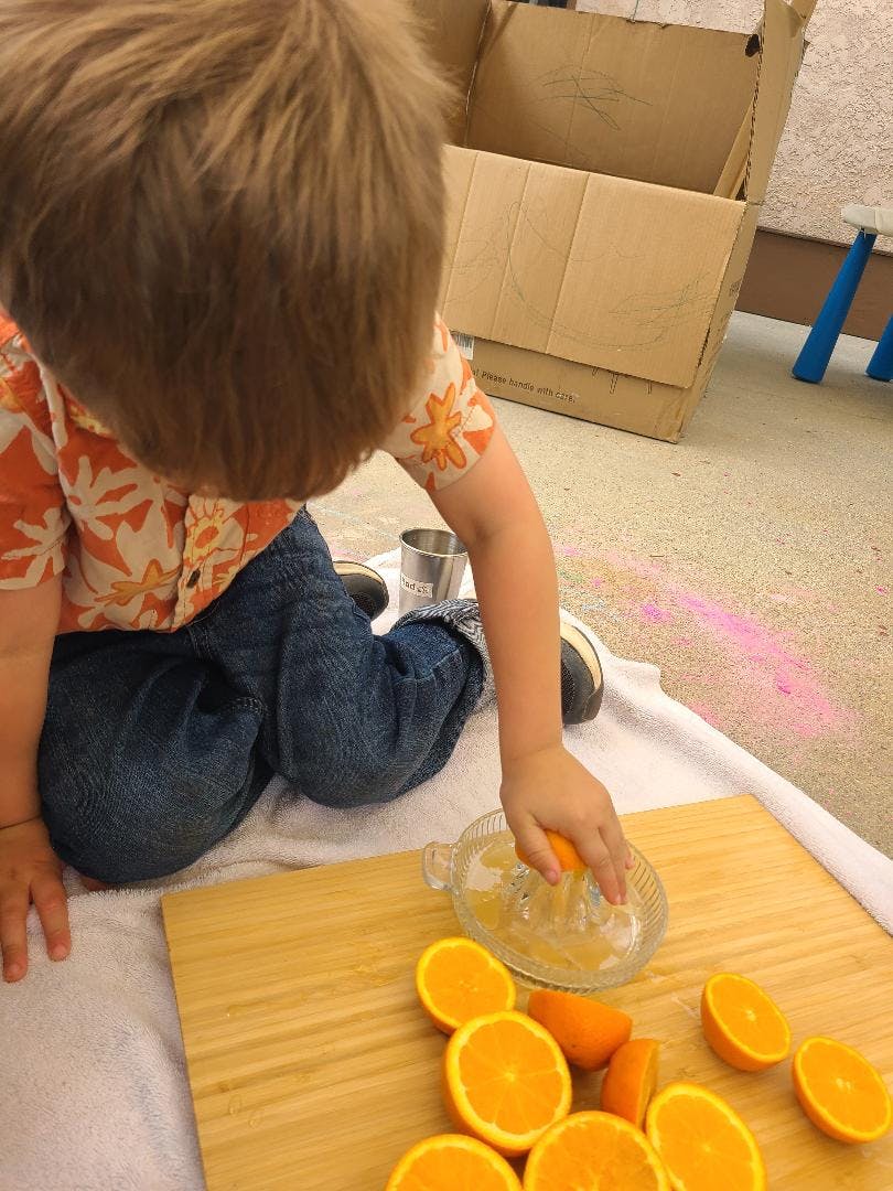 Child squeezing an orange half with a juicer on a cutting board