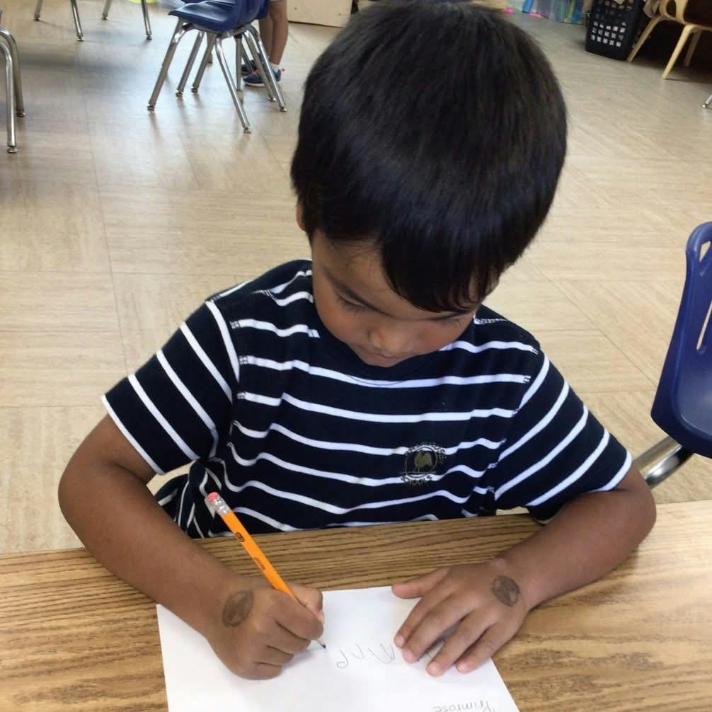 Child writing on paper with a pencil at a desk in a classroom