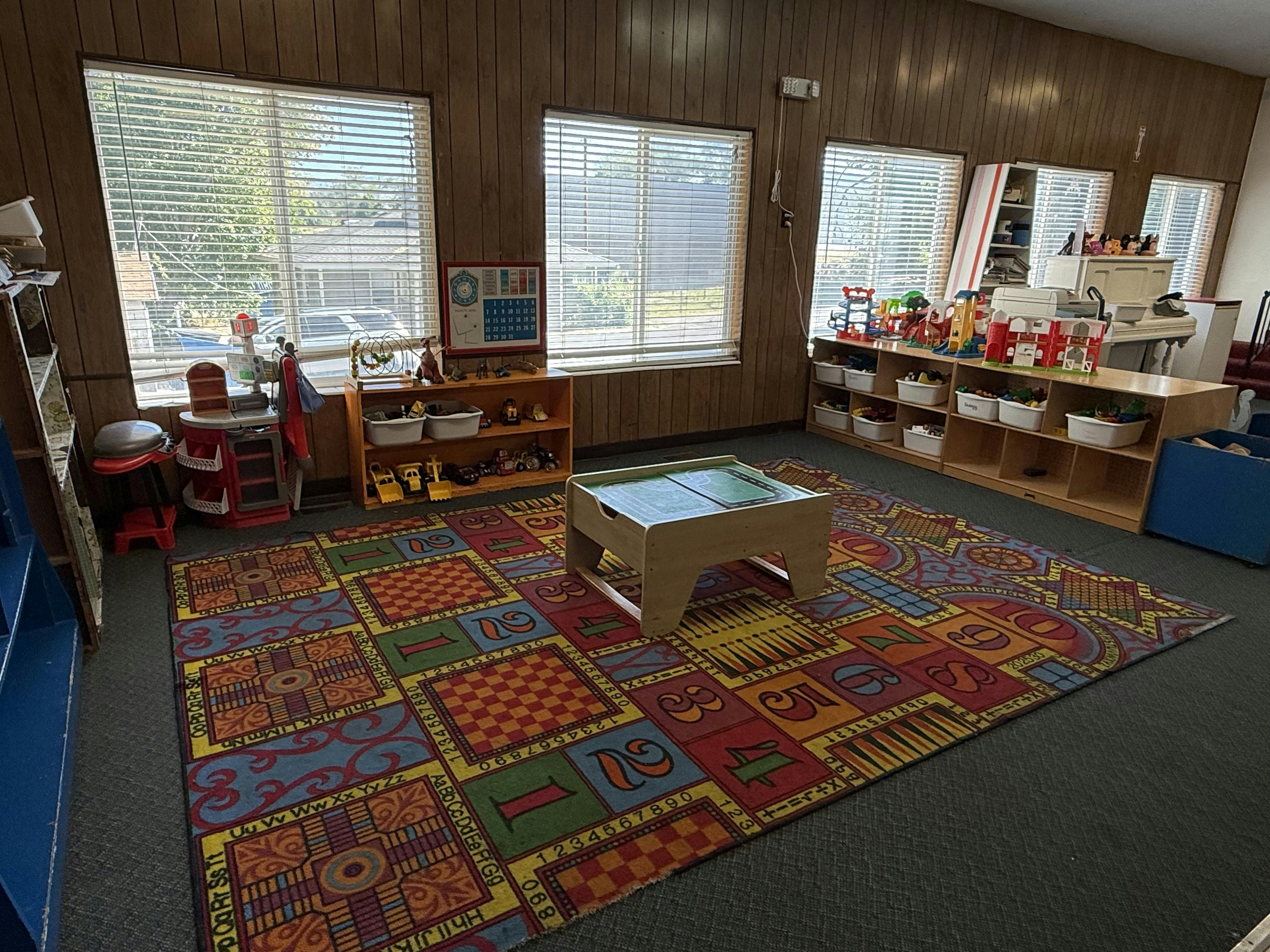 Playroom with colorful rug, small table, and shelves with toys