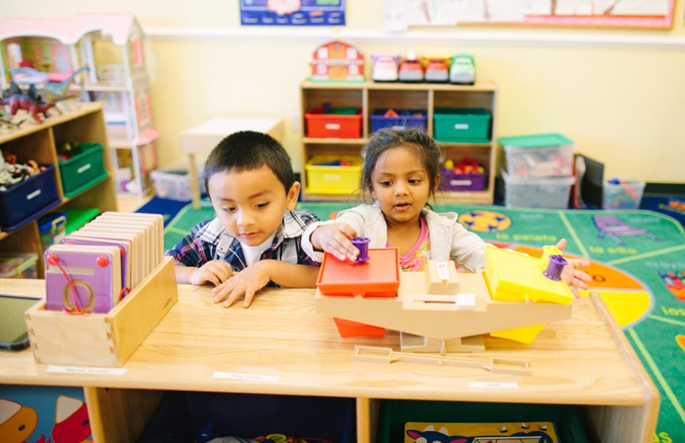 Two children playing with a toy on a table in a classroom