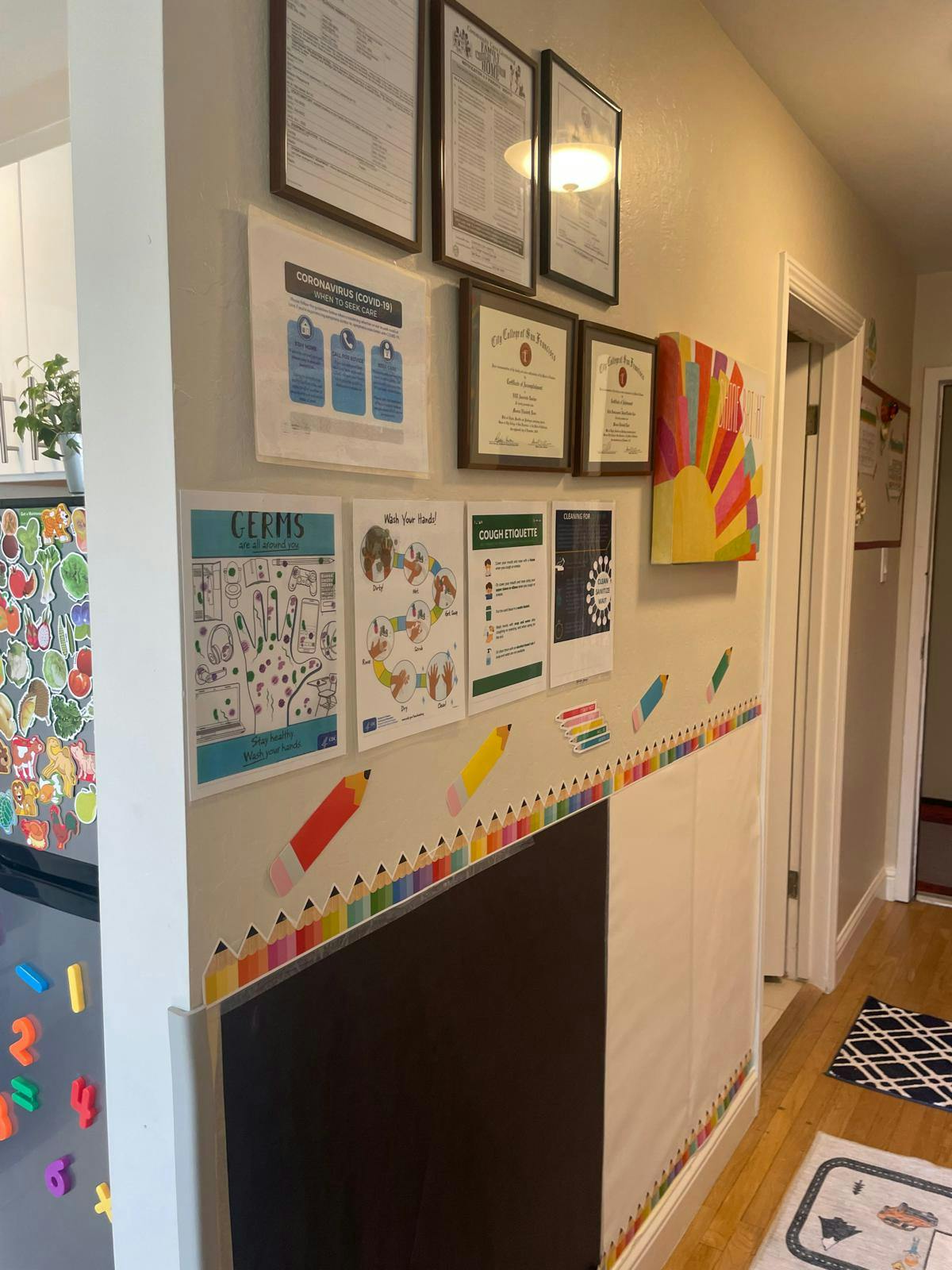 Wall decorated with framed certificates, educational posters, and crayon border
