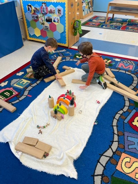 Two children playing with wooden blocks on a rug in a classroom
